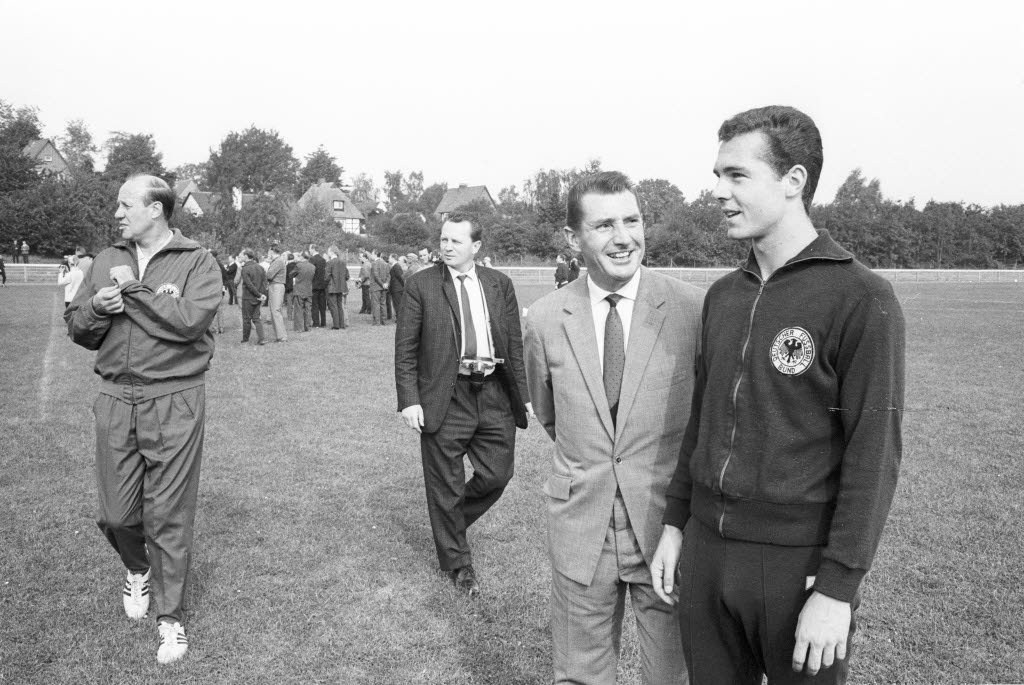 Anno 1965 Im Trainingslager der deutschen Fußball-Nationalmannschaft zu Malente: Fritz Walter (2. v. re.) mit dem jungen Franz Beckenbauer (re.), Bundestrainer Helmut Schön (li.) sowie einem Fotografen. (Foto: Wikimedia Commons / Friedrich Magnussen (1914-1987) / Stadtarchiv Kiel). Link zur Lizenz: https://creativecommons.org/licenses/by-sa/3.0/de/deed.de