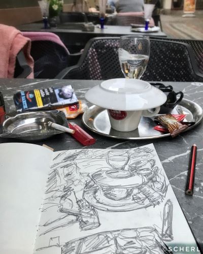 Foto einer Zeichnung in einem Skizzenbuch, dahinter ein Tablett mit einer Kaffeetasse
